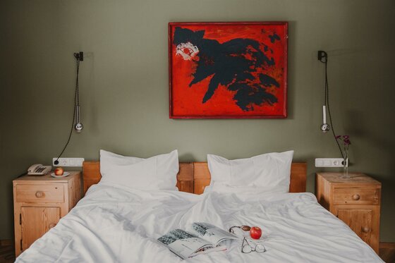 Doppelbett mit weißer Bettwäsche vor grüner Wand mit rotem Gemälde und Holz-Nachttischen.