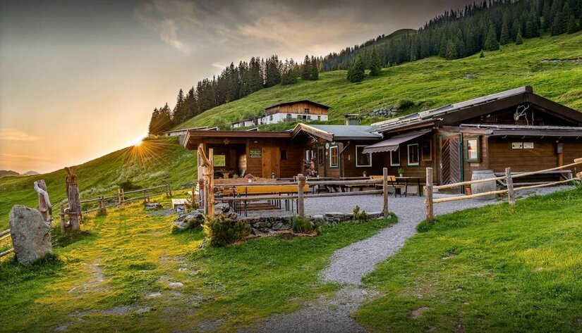 Hochwildalm im Sommer Holzhütte mit Außenterrasse auf einer grünen Almwiese bei Sonnenuntergang.