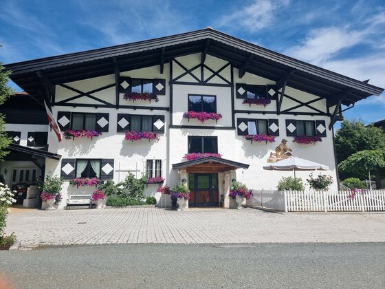 Vorderansicht des Hotel Zimmermann mit weißer Fassade, dunklem Holzgebälk und Blumenkästen unter blauem Himmel.