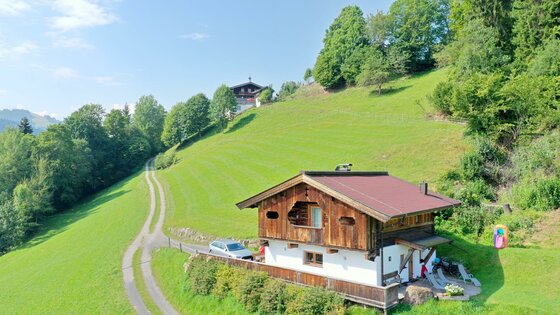 Ein hübsches Holzhaus inmitten grüner Wiesen und Bäume. Der Himmel ist blau und die Landschaft ist ruhig und malerisch.