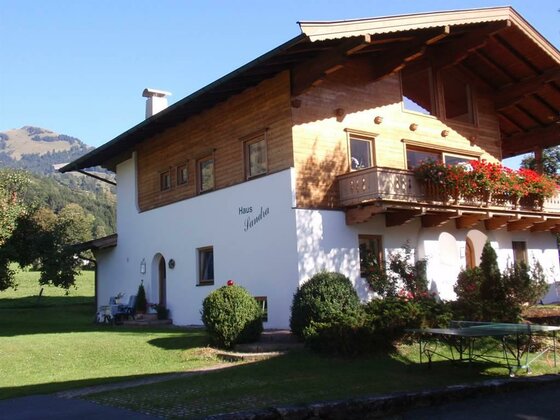 Haus Sandra im Sommer Zweistöckiges Alpenhaus mit Holzfassade, Balkonblumen und Garten vor Bergkulisse.