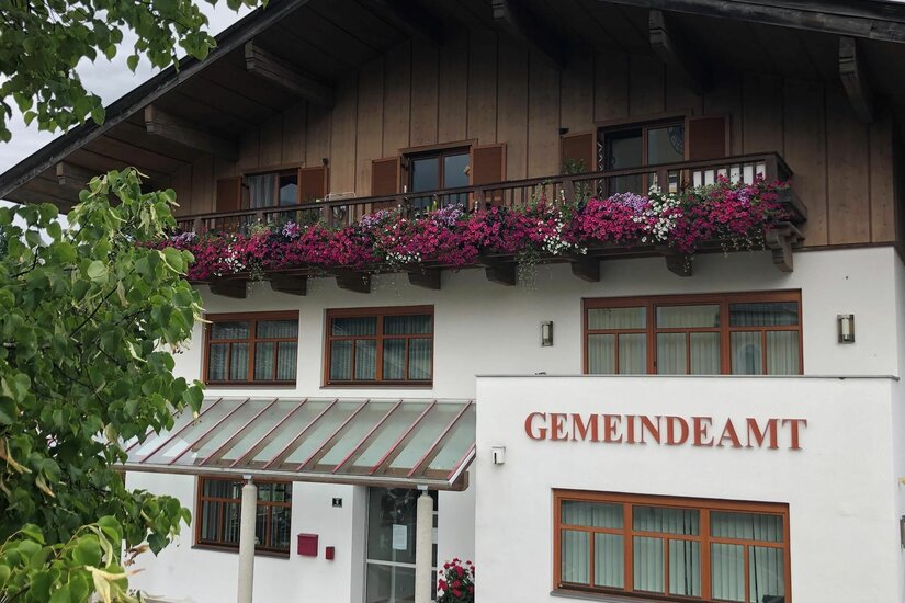 Gemeindeamt Aurach Vorderansicht eines Gemeindeamts mit Holzfassade im Obergeschoss und blumengeschmücktem Balkon.