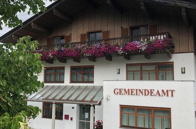 Gemeindeamt Aurach Vorderansicht eines Gemeindeamts mit Holzfassade im Obergeschoss und blumengeschmücktem Balkon.