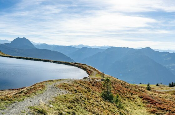 Blick über einen Speichersee am Pengelstein auf die umliegende Berglandschaft bei Tageslicht.