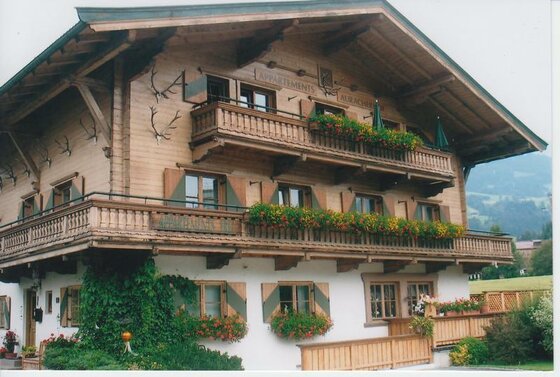 Alpines Holzhaus mit Blumenbalkonen und Geweihen an der Fassade.