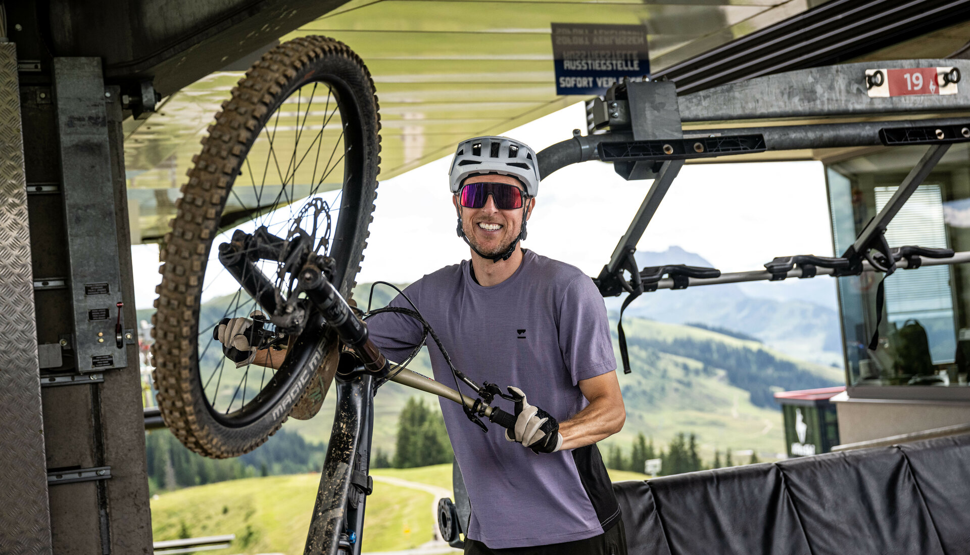 Ein Mountainbiker nimmt sein Fahrrad an einer Liftstation der 360 Flow Trails Kitzbühel vom Bike-Lift, lächelnd und bereit für die nächste Abfahrt.
