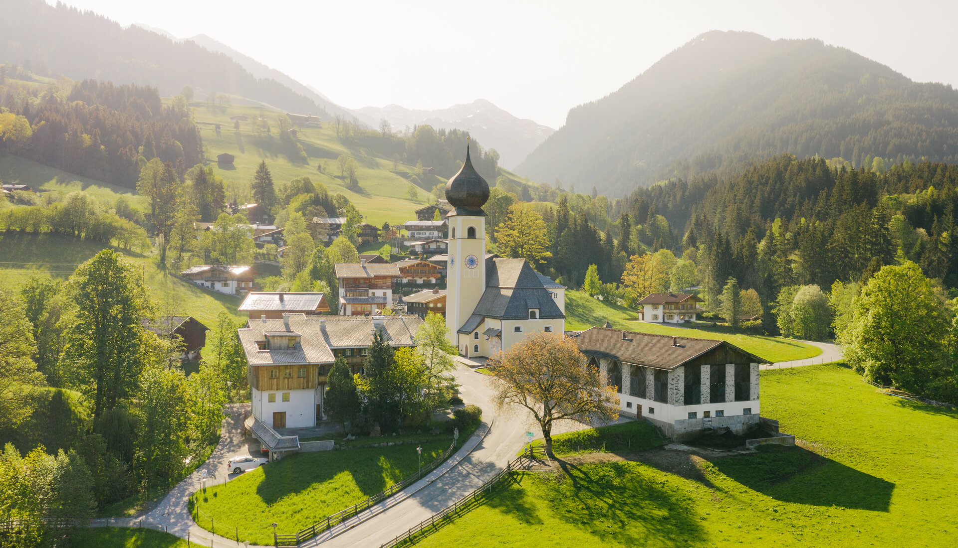 Eine malerische Berglandschaft mit einer charmanten Kirche und traditionellen Häusern, umgeben von grünen Wiesen und Bäumen.