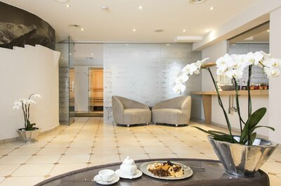 Wellnessbereich im Hotel Reisch Moderner Wellness-Ruheraum mit zwei Sesseln, hellen Fliesen und Orchideen im Vordergrund.