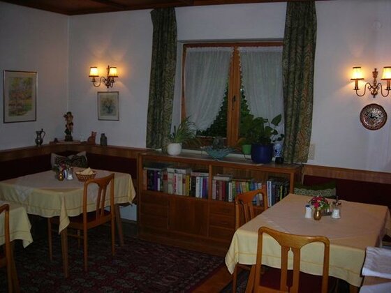 Rustikaler Frühstücksraum mit Holztischen, Stühlen, Eckbank und einem Bücherregal unter dem Fenster.