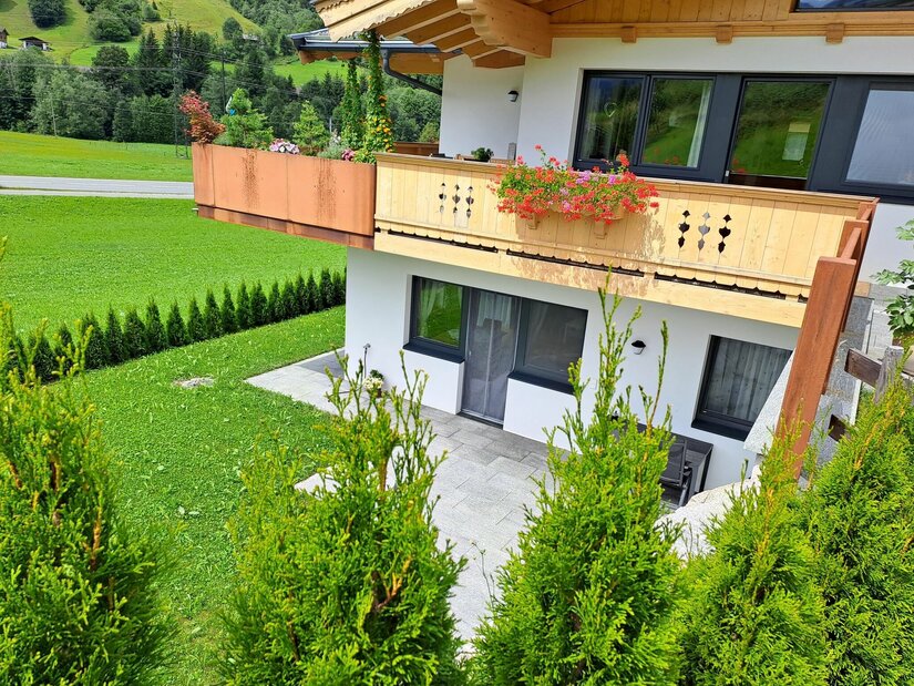 Ferienwohnung Widmann Jochberg Modernes Alpenhaus mit Holzbalon, Terrasse und Gartenanlage vor grüner Bergkulisse.