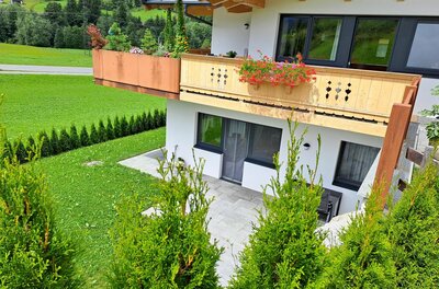 Modernes Alpenhaus mit Holzbalon, Terrasse und Gartenanlage vor grüner Bergkulisse.