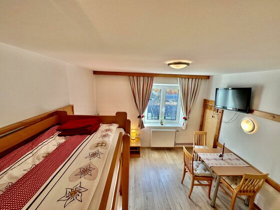 Zimmer in Central Kitz Apartments Innenansicht eines Zimmers mit Holz-Etagenbett, Esstisch und Fernseher.