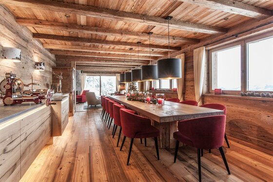 Rustikaler Speisesaal mit langem Holztisch, roten Polsterstühlen und Deckenbalken aus Altholz.