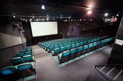 Filmtheater Kitzbühel Ein modernes Kino mit blauen Sitzen und einem großen Bildschirm. Der Raum ist bereit für die nächste Filmvorführung.