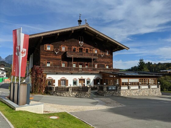 Alpenhaus in Reith Traditionelles Alpenhaus aus dunklem Holz mit weißem Erdgeschoss und rot-weißen Fahnen davor.
