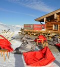 Sonnenterrasse der Bärenbadalm mit roten und grauen Sitzsäcken im Schnee vor einer Holzhütte.