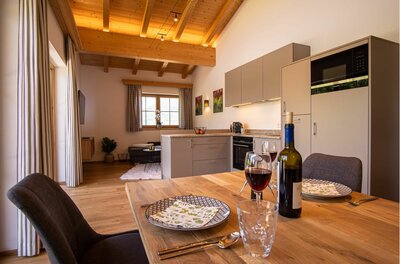 Moderner Wohn-Essbereich mit Holzbalkendecke, Küchenzeile und gedecktem Holztisch mit Weingläsern.