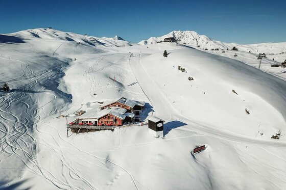 Berggasthaus Resterhöhe im Winter Vogelperspektive auf das Berggasthaus Resterhöhe inmitten einer verschneiten Gebirgslandschaft mit Skipisten.