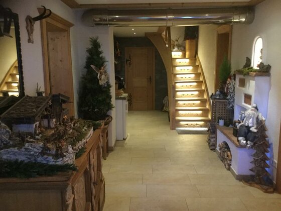 Innenansicht eines Hausgangs mit Steinfliesen, Holztreppe und weihnachtlicher Dekoration.