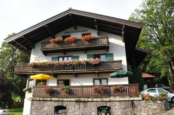 Haus Eugenie in Kitzbühel Dreistöckiges Alpenhaus mit Holzbalkonen und Blumenschmuck unter einem weiten Dachüberstand.