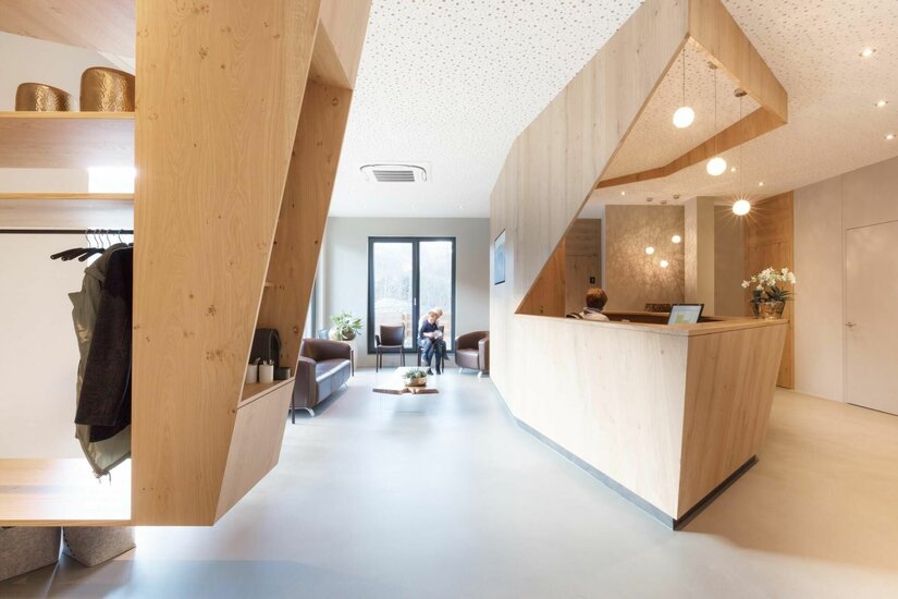 Moderner Empfangsbereich mit hellem Holz-Tresen, Sitzgelegenheiten und Garderobe.