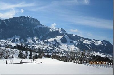 Verschneite Berglandschaft mit einem Dorf im Tal unter blauem Himmel.