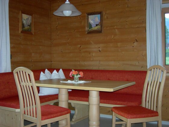 Essecke mit Holztisch, roter Eckbank und zwei Stühlen in einer holzgetäfelten Stube.