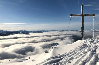 Gipfelkreuz am Hochetzkogel Gipfelkreuz auf dem verschneiten Hochetzkogel über einer geschlossenen Wolkendecke unter blauem Himmel.