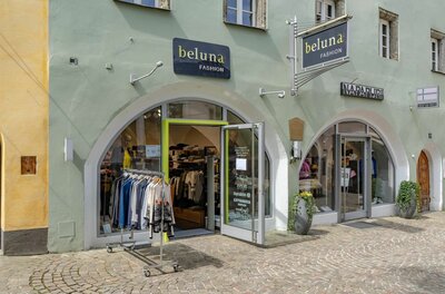 Beluna Fashion Ladengeschäft Außenansicht des Modegeschäfts Beluna Fashion mit zwei Rundbogen-Eingängen und Kleiderständer auf Kopfsteinpflaster.