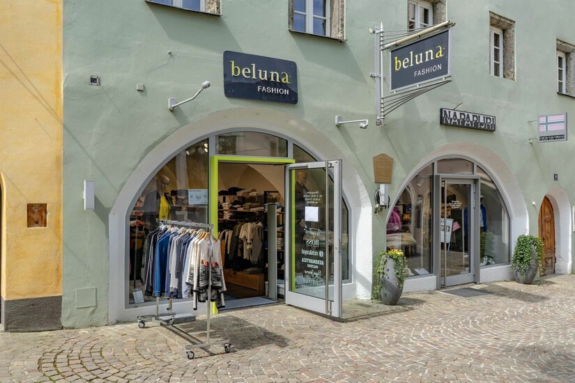 Außenansicht des Modegeschäfts Beluna Fashion mit zwei Rundbogen-Eingängen und Kleiderständer auf Kopfsteinpflaster.