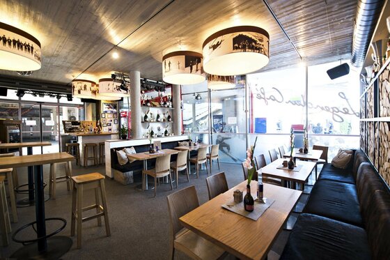 Innenansicht eines Cafés mit Holztischen, Sitzbänken und runden Hängelampen mit historischen Skimotiven.