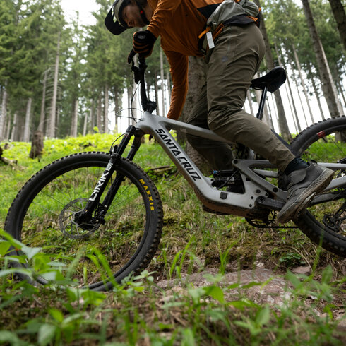 Ein Mountainbiker fährt bergauf auf einem Singletrail bei den 360 Flow Trails in Kitzbühel durch einen grünen Wald, umgeben von hohen Bäumen und üppigem Gras.