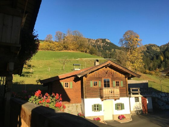 Bauernhof Sinnersberg Hausansicht Traditionelles Holzhaus mit Balkon vor grünen Almwiesen und bewaldeten Bergen unter blauem Himmel.