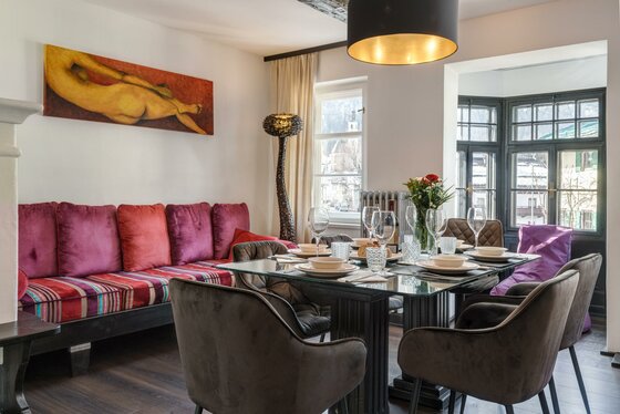 Esszimmer Hornbichl Moderner Essbereich mit Glastisch, dunklen Polsterstühlen, einer bunten Sitzbank und einem großen Wandgemälde.