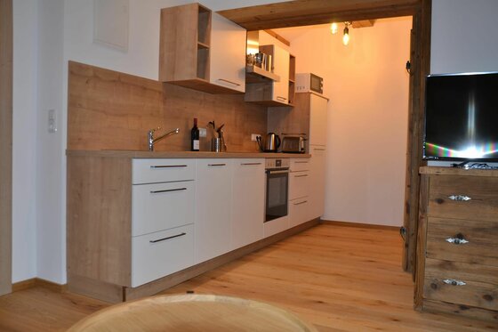 Moderne Küchenzeile mit weißen Fronten, Holz-Arbeitsplatte und eingebauten Elektrogeräten in einer Ferienwohnung.