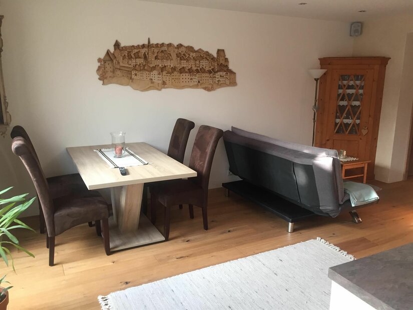 Esstisch im Appartement Lyso Ein Esstisch mit vier braunen Stühlen neben einem grauen Sofa in einem hellen Wohnraum.