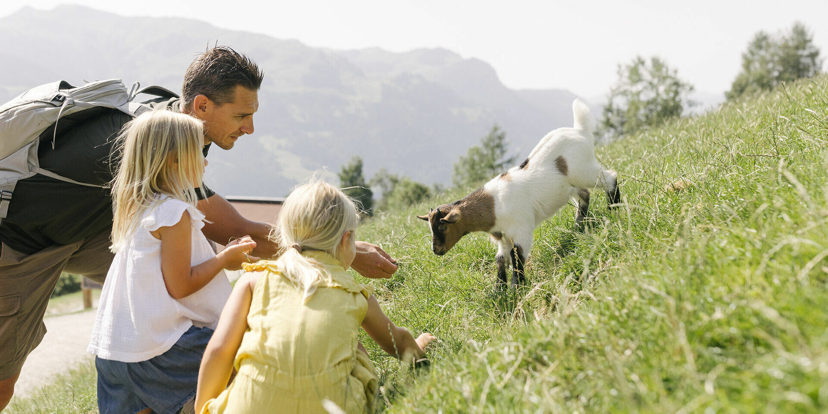 Vater und zwei Töchter füttern ein Ziegenjunges im Wildpark Aurach bei Kitzbühel.
