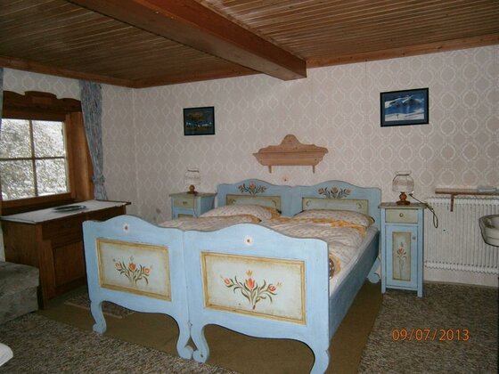 Das blaue Zimmer im Plattenhof Rustikales Schlafzimmer mit zwei hellblauen Holzbetten mit Blumenmalerei und Holzdecke.
