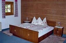 Doppelzimmer im Martenhof Rustikales Doppelbett aus Holz vor einer Holzwand mit zwei Nachttischen und einem kleinen Fenster.