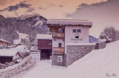 Schneebedecktes mehrstöckiges Ferienhaus mit Holzbalkonen vor bewaldeten Bergen im Winter.