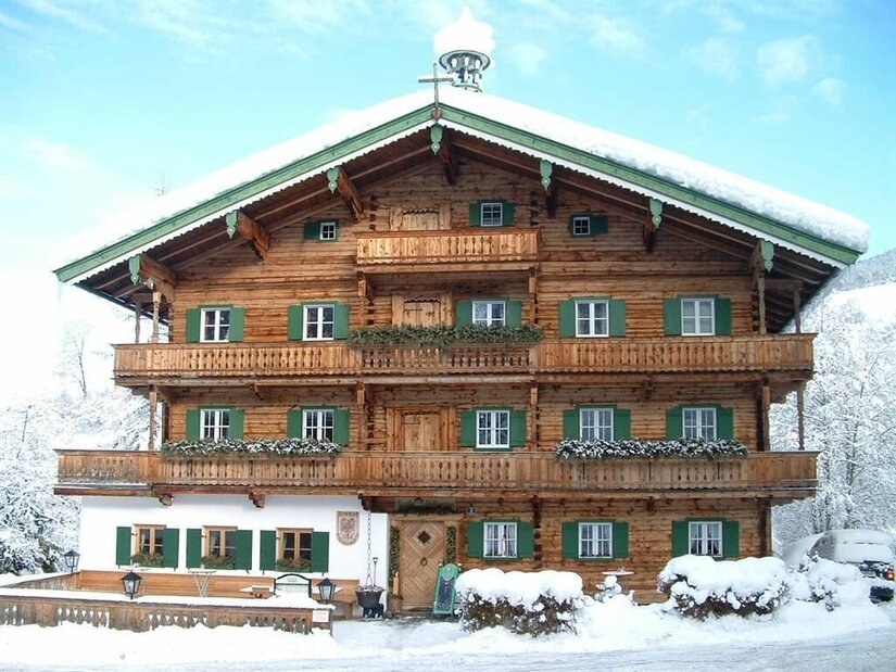 Mehrstöckiges Holzhaus im alpinen Stil mit grünen Fensterläden und schneebedecktem Dach im Winter.