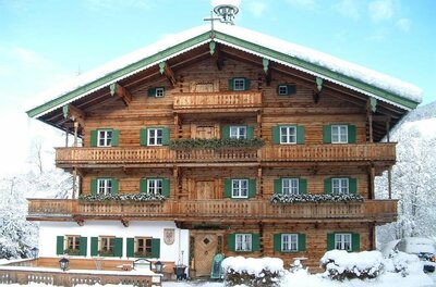 Mehrstöckiges Holzhaus im alpinen Stil mit grünen Fensterläden und schneebedecktem Dach im Winter.