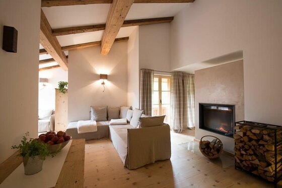 Moderner Wohnraum mit Ecksofa, Holzbalkendecke, Kamin und Brennholzregal.