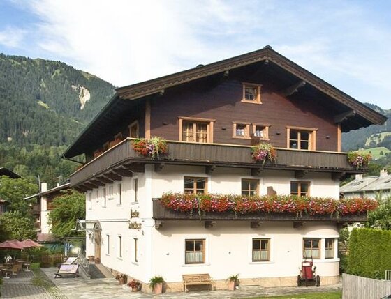 Dreistöckiges alpines Gästehaus mit Blumenbalkonen vor bewaldeten Bergen.
