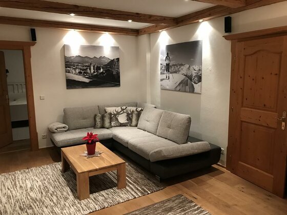 Wohnzimmer mit grauem Ecksofa, Holztisch und Bergfotografien an der Wand.