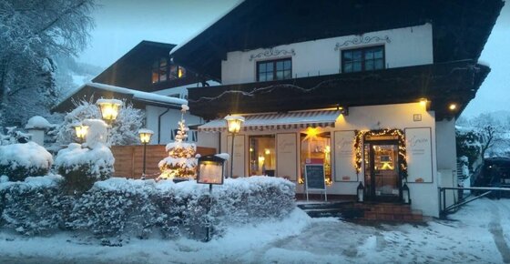 Ein verschneites Gasthaus bei Dämmerung mit beleuchteten Fenstern und Weihnachtsdekoration.