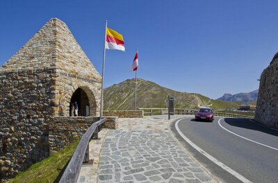 Steinerner Turm am Fuscher Törl neben der Großglockner Hochalpenstraße mit Flaggen und einem Auto.