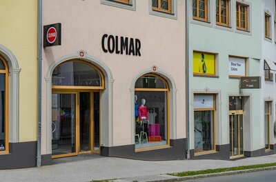 Außenansicht eines Sportgeschäfts mit Schaufenstern und Colmar-Schriftzug an einer hellen Fassade.