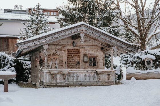 Haus Gantschnigg im Winter Kleine Holzhütte mit schneebedecktem Satteldach und verzierten Balken in einer Winterlandschaft.