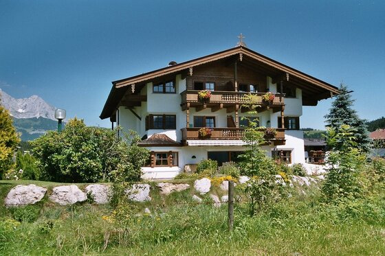 Gästehaus Ponapart Dreistöckiges alpines Gästehaus mit Holzbalkonen, Blumenkästen und Garten vor Bergkulisse.